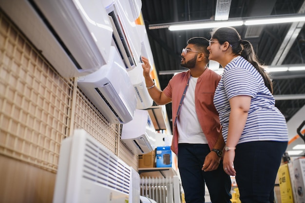 young-indian-couple-satisfied-customers-choosing-air-conditioner-appliances-store